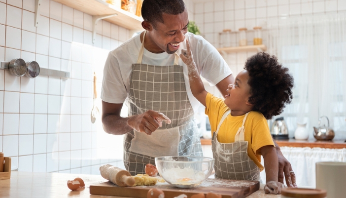 A father and son play around while making cookies in their kitchen.