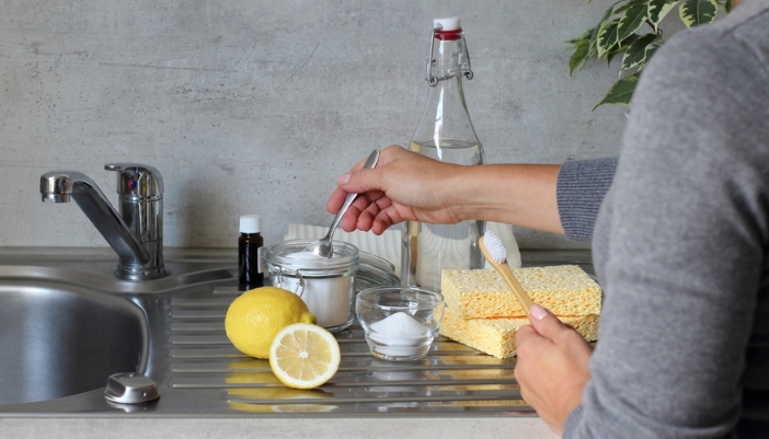 A pair of women’s hands puts together cleaning supplies with lemon, baking soda, and more.