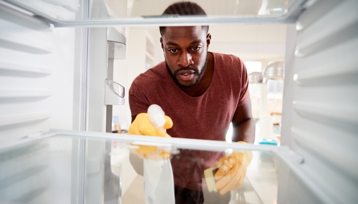 A man sprays into his fridge to clean the glass shelves.