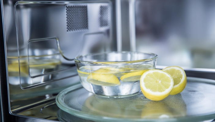 A clear bowl with water and lemons sits in a microwave.