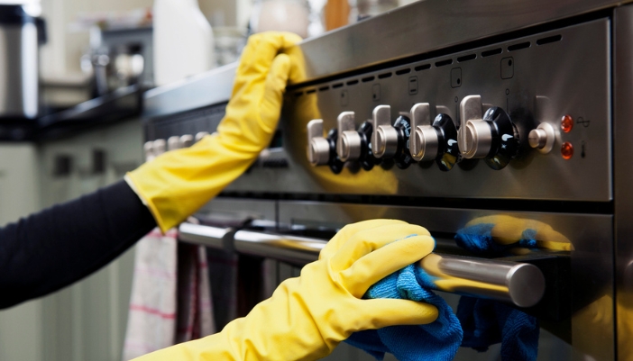 A pair of yellow gloved hands wipe down the outside of an oven.