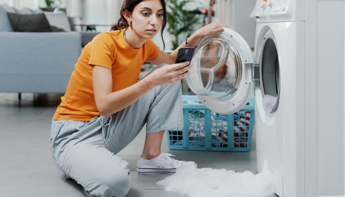 A woman uses her phone to look up why her washer is overflowing with suds.