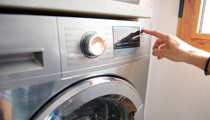 A hand changes the settings on a washing machine.