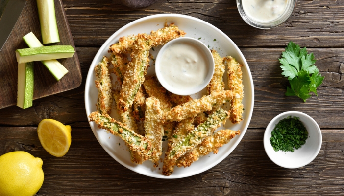 Air fried zucchini fries sit on a white bowl on a wooden background.