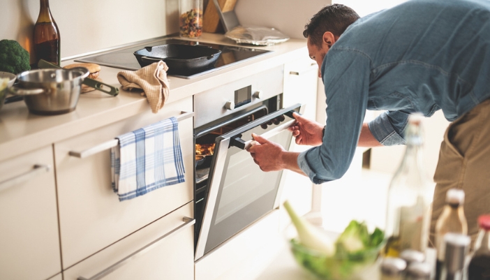 A man cracks open his oven to check on the food inside.
