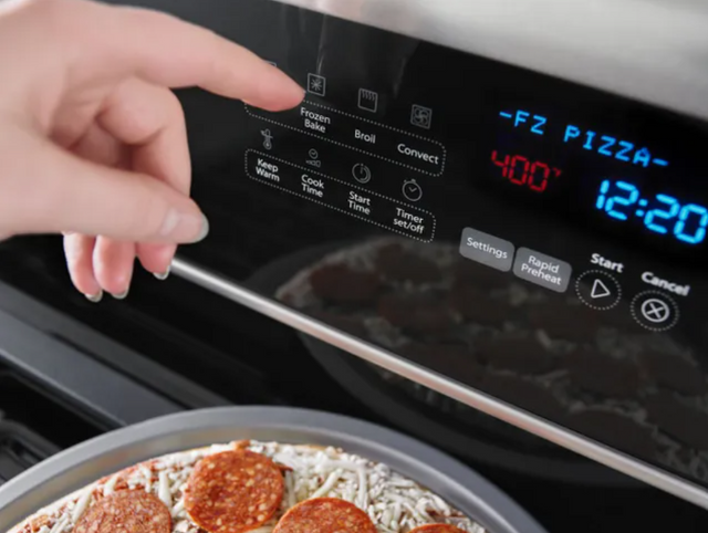 close view of a hand pressing a control button on their whirlpool electric range, with a pizza sitting out of shot on top of the range