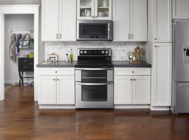 front view of a modern kitchen with white walls and white cabinetry, showing a stainless steel double oven electric range and over the range microwave from whirlpool