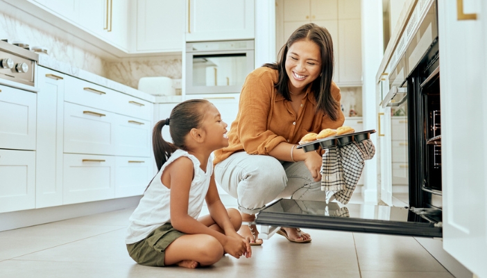 A woman and child remove a tray from their kitchen’s oven.
