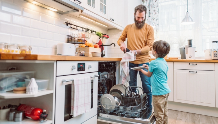 A father and son unload a dishwasher in their family’s kitchen.