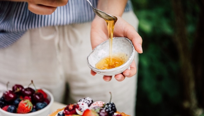A woman’s hand drips honey onto a fruit tart.