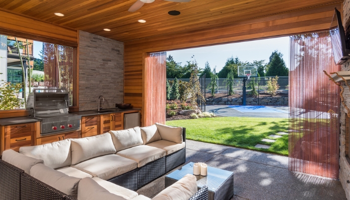 A covered patio with white furniture, sliding doors, and an outdoor kitchen.