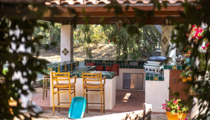 A boho, Moroccan inspired backyard outdoor kitchen with green tile and a pergola.
