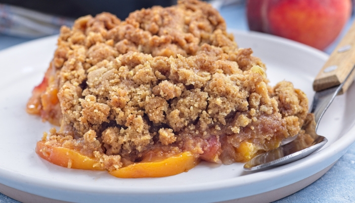 A closeup of a slice of peach crumble on a white plate.
