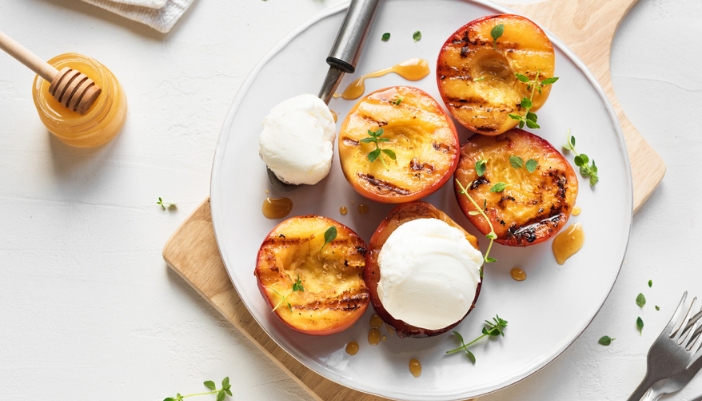 A plate of grilled peaches with cream and some honey.