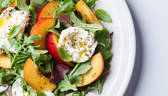 A closeup of a salad with peaches and soft cheese.