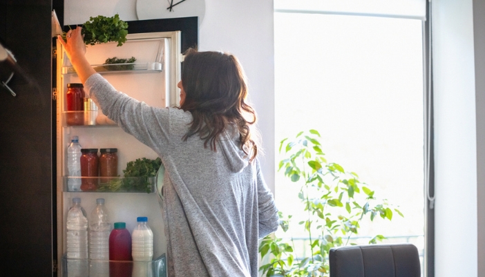 A woman reaches into her open refrigerator. 