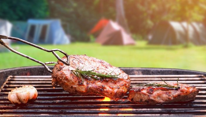 A pair of tongs flips a steak on an outdoor grill. 