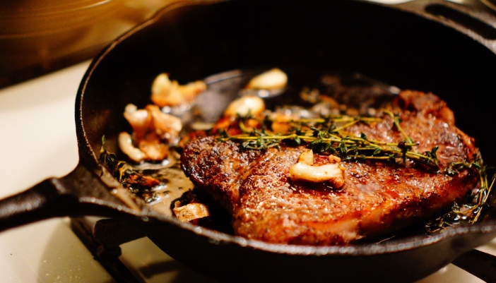 closeup of a steak in a cast iron pan with garlic and herbs surrounding.