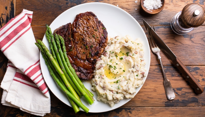 A rustic plate setting with a cooked steak, asparagus, and mashed potatoes on a plate.