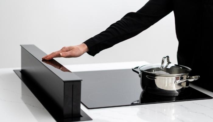 someone reaching to turn on sleek black downdraft ventilation unit