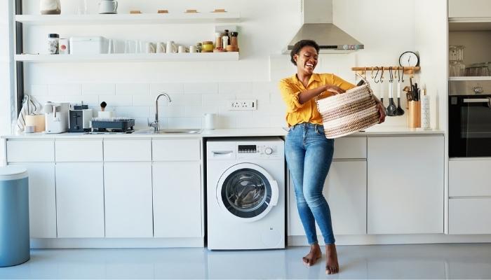 young African American woman smiling in laundry room holding laundry basket