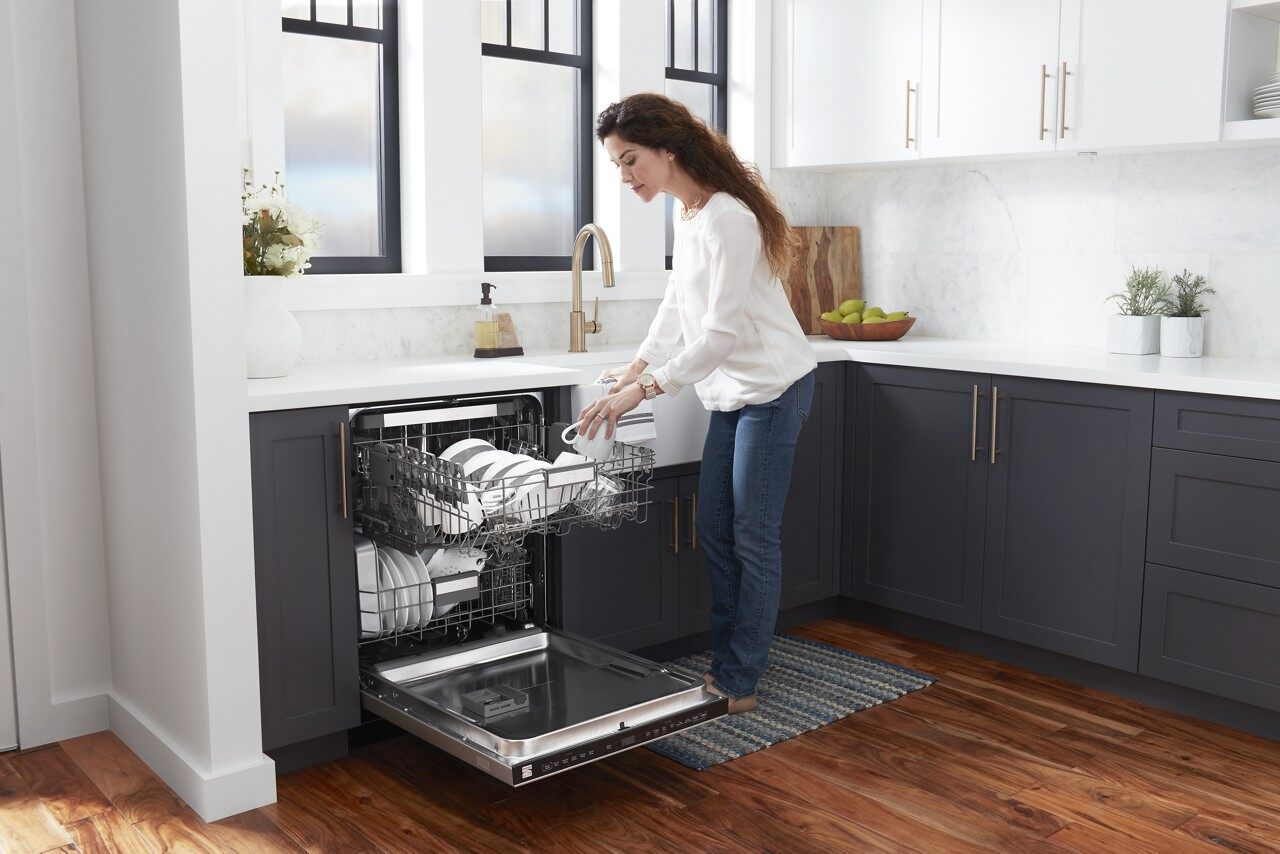 Front view of a woman loading a stainless steel dishwasher in a modern kitchen