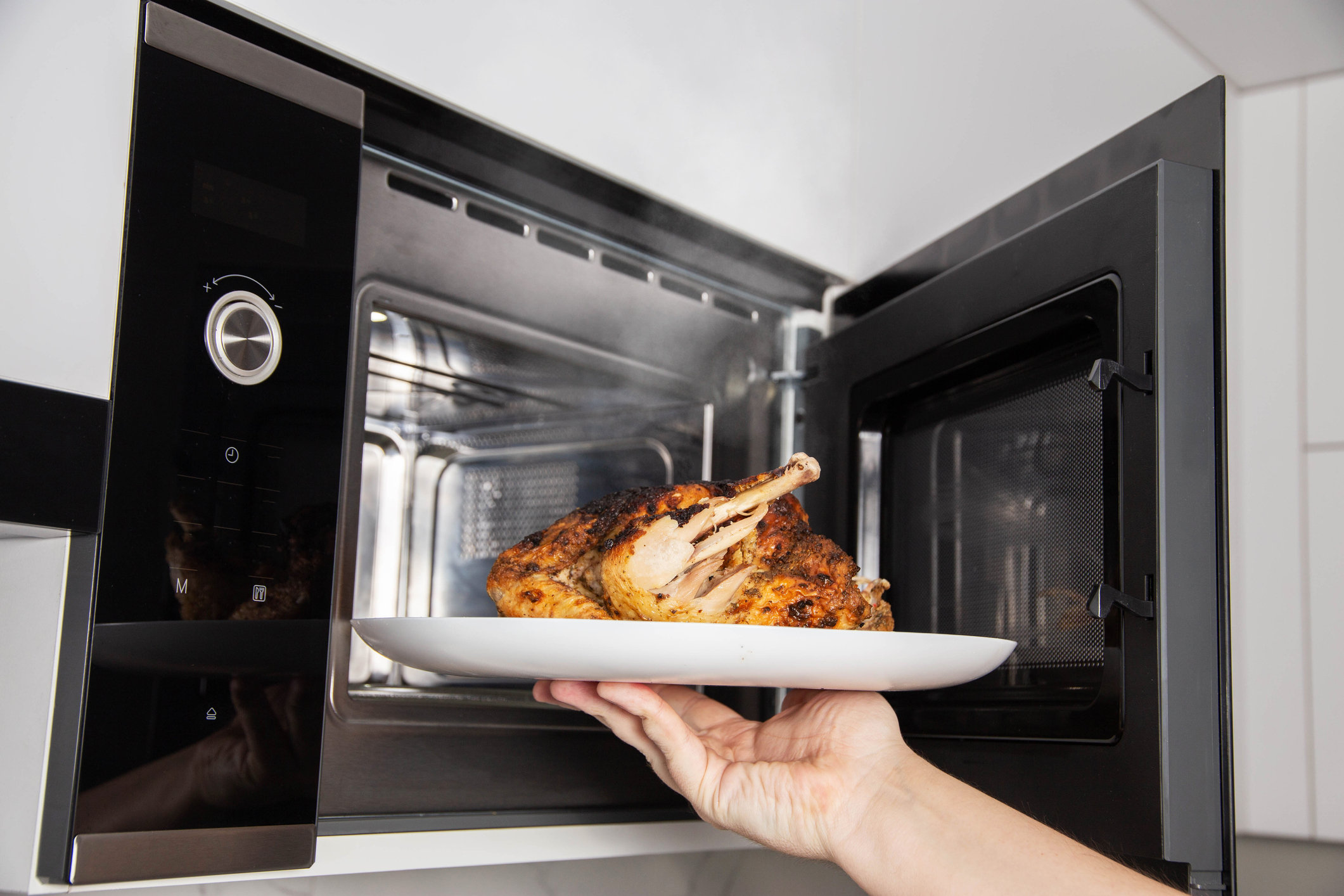 man taking plate of grilled chicken out of microwave oven 