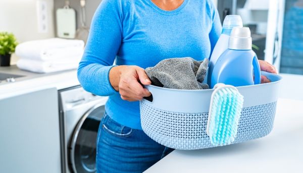 A woman holds a basket of laundry with bottles of detergent and softener