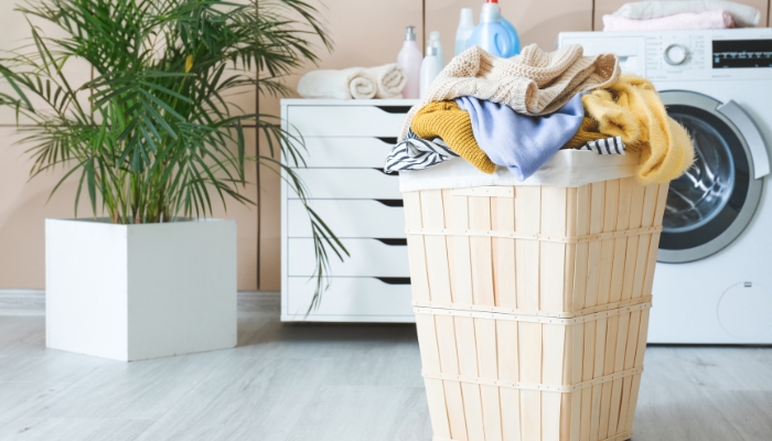 Closeup of a basket of laundry with detergent and other laundry bottles in the background next to a washer machine