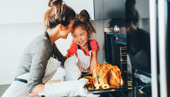 A mother and daughter pull a golden turkey out of a black oven.