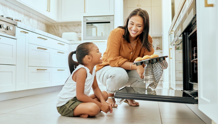 A mom and daughter take their cupcakes out of an open oven.