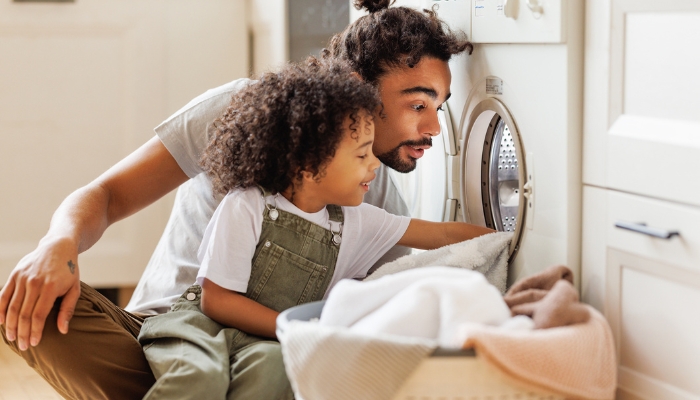 A man and his son empty clothes out of a dryer together.