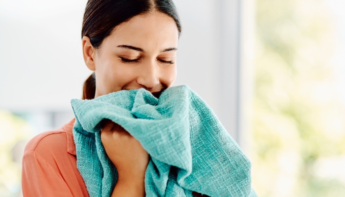 A woman holds a blanket up to her nose and smells it happily.
