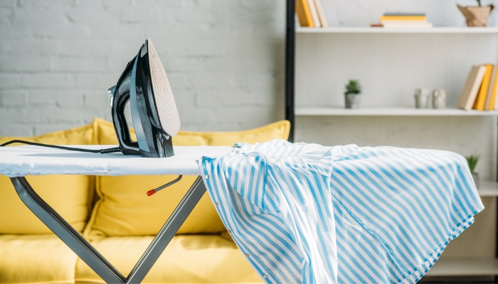 An iron sits on an ironing board next to a striped blue shirt.