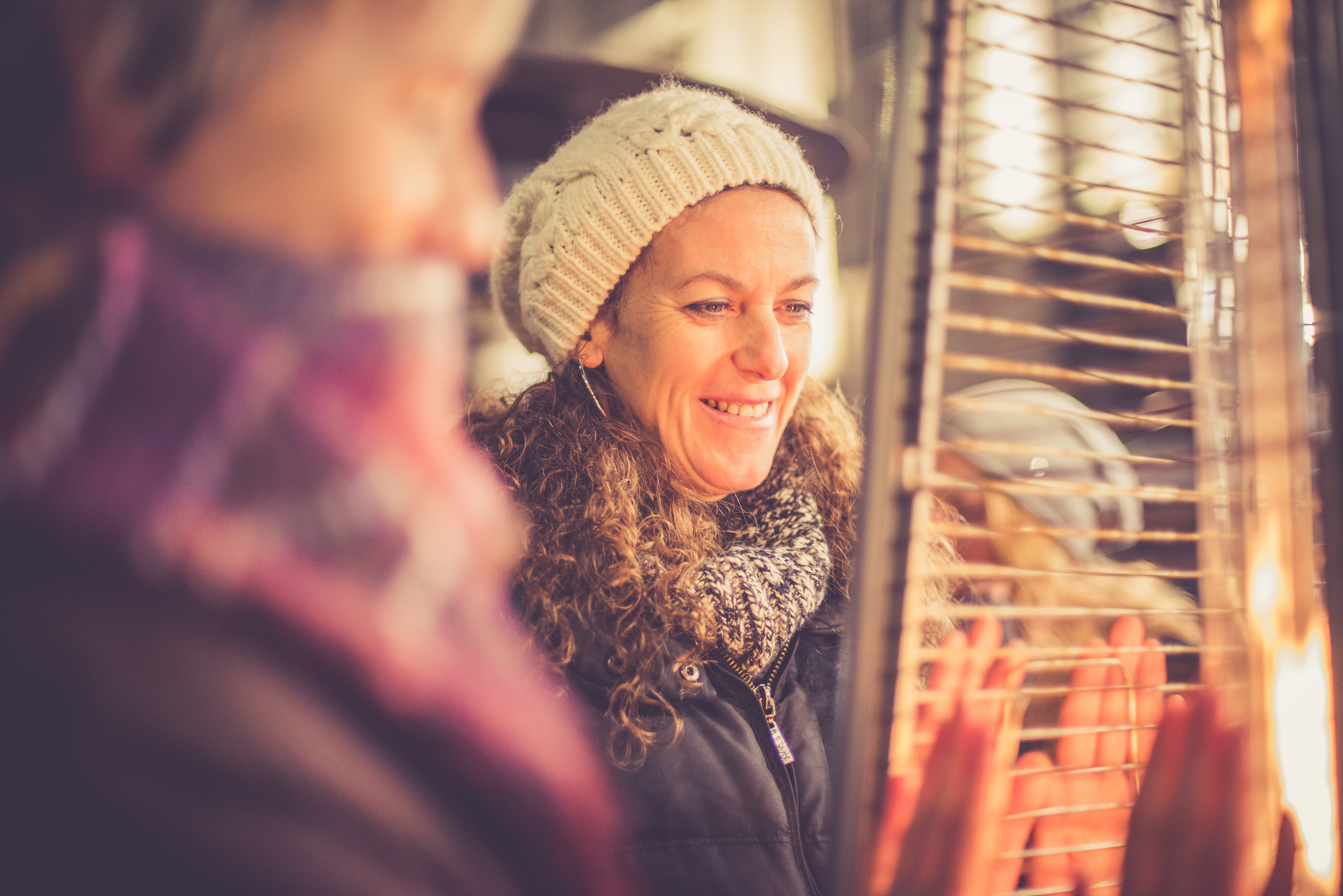 closeup of woman and friend warming up at outdoor heater