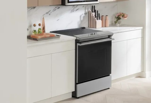 view of a kitchen with a cage induction range between white cabinets and marble countertops, in front of a marble backsplash 