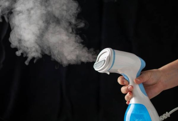 view of a hand holding a handheld clothes steamer blowing steam in front of a black backdrop