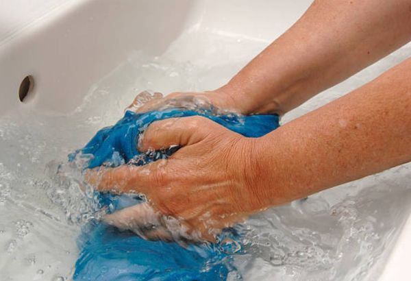 person's arms hand-washing a blue shirt in a sink