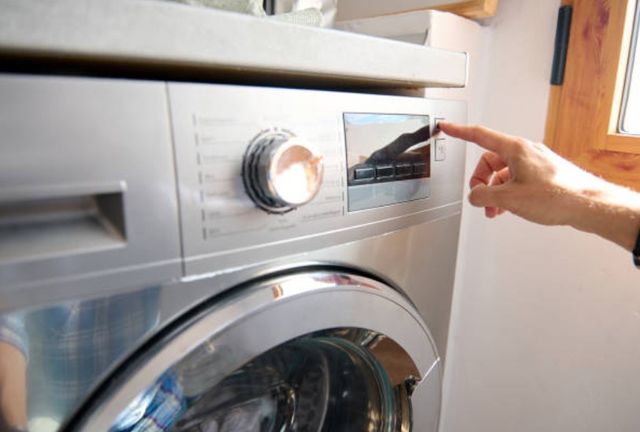 closeup of the control panel on a washing machine, with a hand pointing a finger to press a button