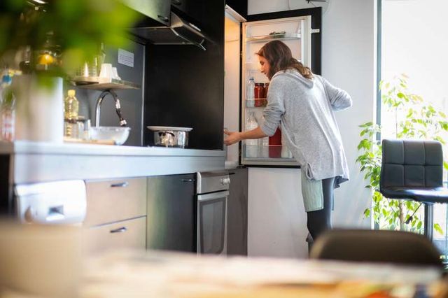 side view of a woman opening her refrigerator in a modern kitchen
