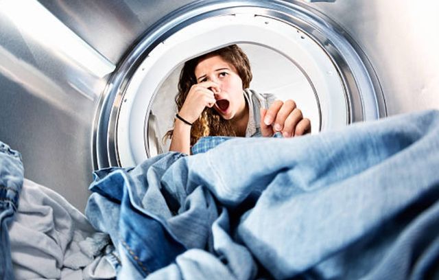 woman holding her nose while opening a washing machine