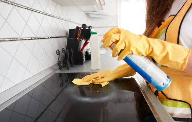woman wearing yellow gloves and apron cleaning glass cooktop