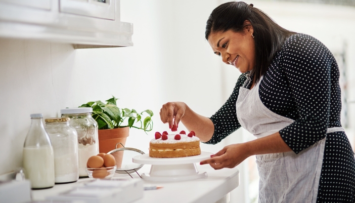 A woman in an apron is decorating her cake with strawberries around the top