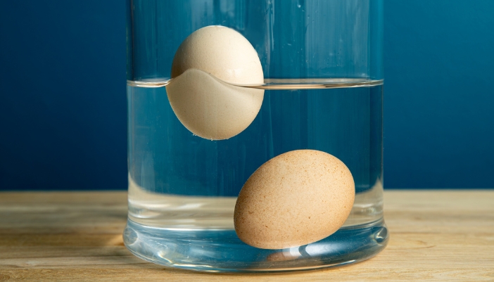 Two eggs in a glass of water with one sunk and the other floating indicating freshness
