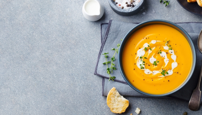 A bowl of pumpkin soup sits on a gray napkin and a gray table.