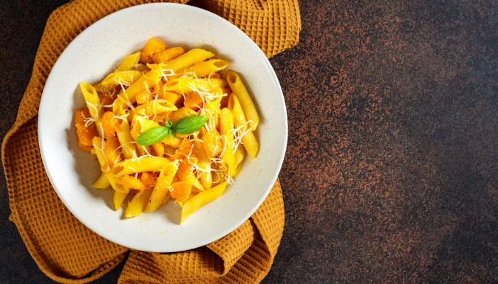 A full bowl of pumpkin-sauce penne pasta on a yellow napkin. 