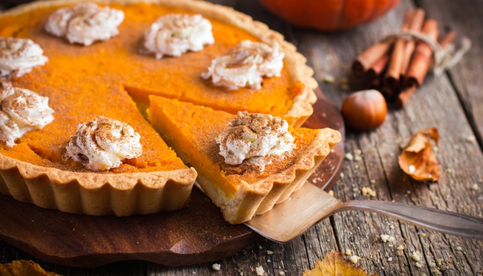 A fresh pumpkin pie on a wooden table and a spatula removing a piece.
