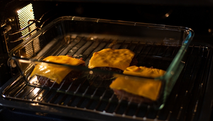 A glass pan in an oven with three cheeseburgers inside.