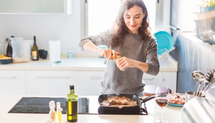 A young woman cooks meat in a grill pan on her stove.