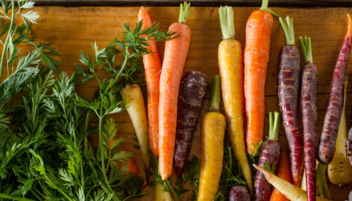 Orange, yellow, and purple carrots laying on a wooden surface.